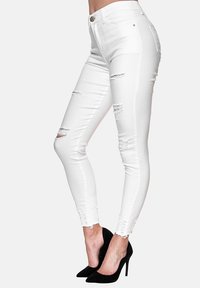 Pantalones vaqueros blancos ajustados con desgarros desgastados, cintura alta y un dobladillo deshilachado. Presentan una tela suave y texturizada y una silueta ajustada.