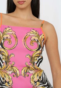 Top senza maniche rosa con ornati motivi zebrati dorati e neri, con spalline arancioni e una texture liscia e setosa.