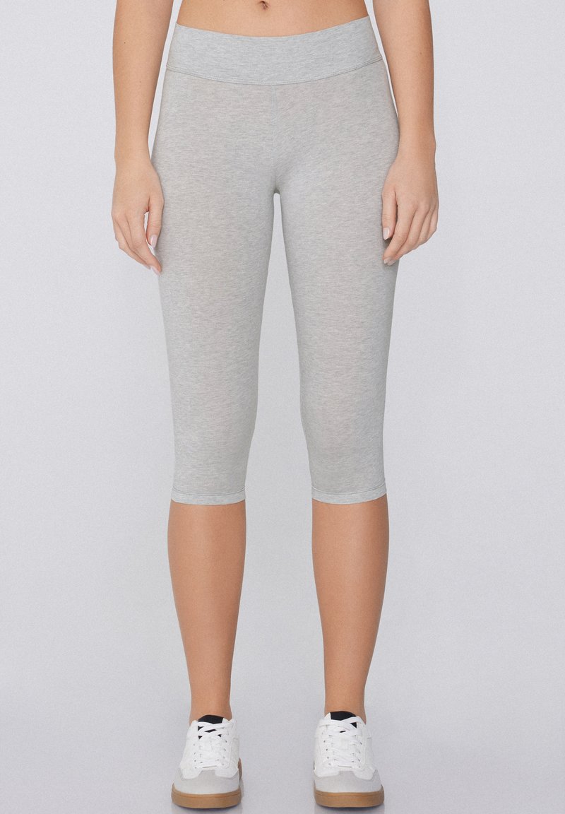 Szare legginsy capri z szerokim, elastycznym pasem. Wykonane z miękkiego, elastycznego materiału, sięgającego do połowy łydki, w zestawie z białymi sneakersami.