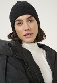 Black ribbed knit beanie paired with a black padded jacket and white turtleneck. Smooth fabric textures and contrasting colors enhance visual appeal.