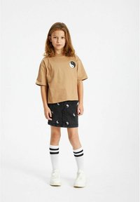 Tricou din bumbac bej cu un grafic yin-yang, asortat cu o fustă din denim negru care prezintă modele repetate de yin-yang, ciorapi albi până la genunchi și adidași.