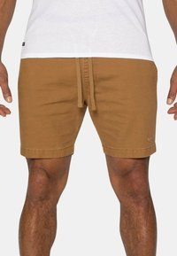 Brune shorts i bomuldsstof, knælange, med elastisk talje og snor, samt subtile logo detaljer nær kanten.