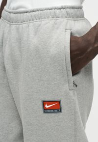 Γκρι φόρμες από απαλό ύφασμα, με ελαστική μέση, πλαϊνές τσέπες και κόκκινο-μπλε λογότυπο Nike.