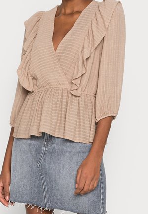 Beige ruffled bluse med dyb V-hals, plisseret talje og struktureret stof. Kombineret med en lys denim nederdel med en frynset kant.