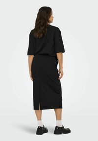 Zwarte, oversized t-shirt en een aansluitende rok met een zijsplit. Draagt witte enkelsokken en chunky zwarte schoenen. Soepele stofstructuur.