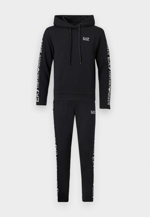 Juodas džemperis su kapišonu ir derančios sportinės kelnės, baltu užrašu „EA7 Emporio Armani“ ant rankovių ir kelnių kojų.