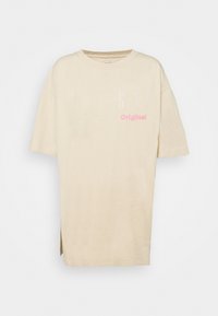 Camiseta oversized beige de algodón, con cuello redondo y slits laterales. Impresos en blanco y rosa están "GAP" y "Original".