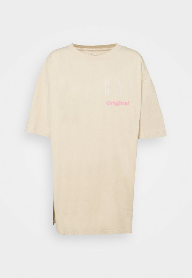 Camiseta oversized beige de algodón, con cuello redondo y slits laterales. Impresos en blanco y rosa están "GAP" y "Original".