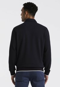 Donkerblauwe pullover met een gestructureerde afwerking, geribde mouwen en een witte accent aan de zoom. Heeft een klassieke kraag en een eenvoudig ontwerp.