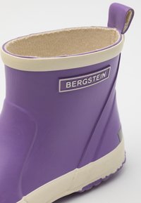 Fioletowy gumowy but Bergstein z beżowym wykończeniem i materiałową podszewką, pokazujący górną stronę oraz tylną pętlę do ściągania na białym tle.
