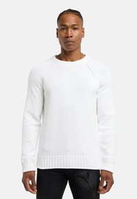 Hvid strikket sweater med ribstrikkede manchetter og kant. Har en rund halsudskæring og diskret branding på skulderen. Glat tekstur.