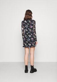 Vestido mini floral con fondo negro, mangas largas y transparentes, y un dobladillo acampanado. Presenta estampados florales coloridos y una silueta ajustada.