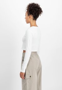 Hvit langermet cropped skjorte med rund utringning, kombinert med beige cargo bukser med elastisk midjebånd og sidelommer.