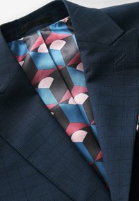 Marineblauwe geruite blazer met een gladde, geometrisch patroonvoering in tinten roze, blauw en zwart. Voorzien van scherpe revers en een enkele pocket.