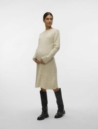 Krämbågad stickad klänning med långa ärmar, midikjolslängd, tillsammans med knähöga svarta läderstövlar. Modellen håller en synlig babybula.