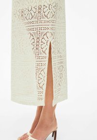 Robe midi en crème clair avec un motif en dentelle et une fente sur le côté. Design à découpes détaillées et ourlet festonné. Association avec des sandales à talons beiges.