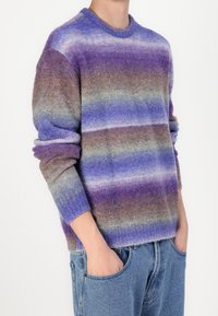 Pull en maille dans des tons de violet, lavande et gris avec des rayures horizontales. Il présente un col rond et des poignets côtelés ; tissu doux et texturé.