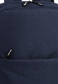 Sac à dos en tissu bleu foncé avec une surface texturée, présentant une étiquette de logo visible et des compartiments zippés. La construction durable est évidente.