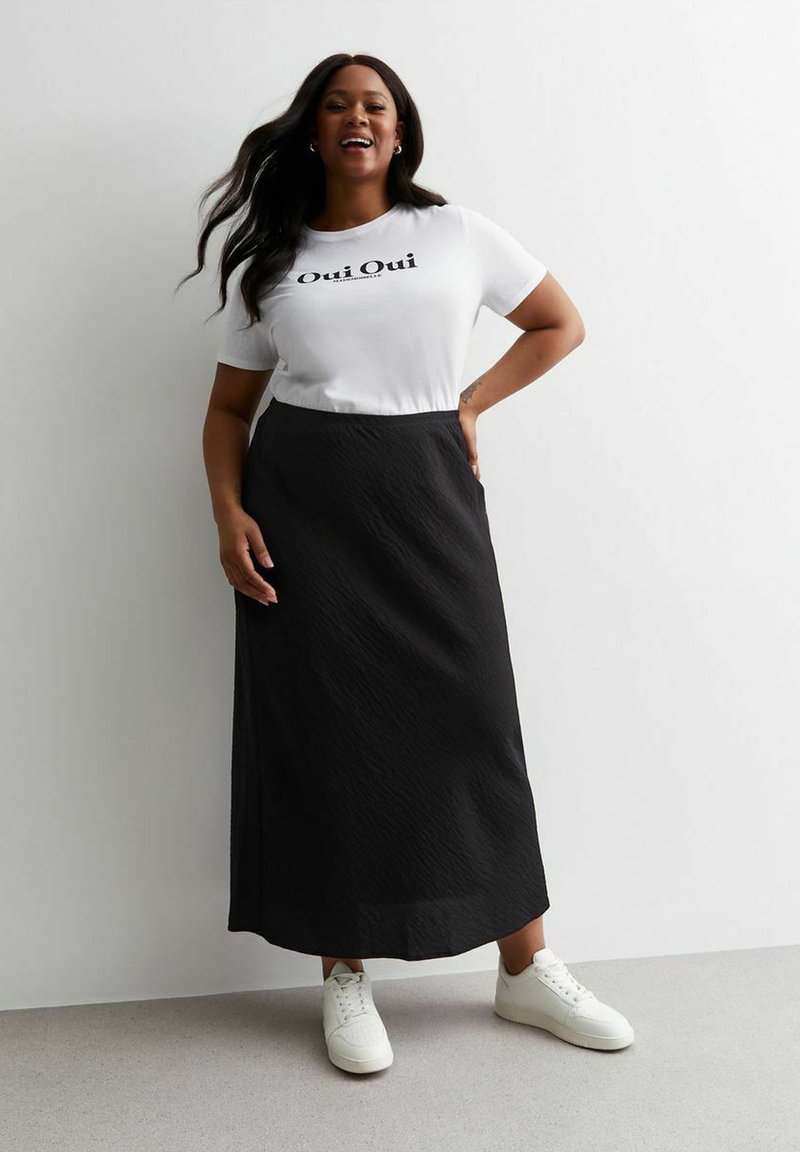 T-shirt en coton blanc avec le texte "Oui Oui", associé à une jupe maxi noire, terminé avec des baskets blanches ; tissu lisse et coupe décontractée.