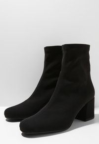 Par de botas negras hasta el tobillo con tacones de bloque y punta redondeada, hechas de un tejidos suaves y elásticos.