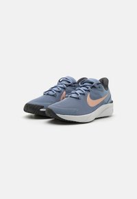 Baskets de sport bleues avec une tige texturée, swoosh Nike rose, accents noirs et une semelle intermédiaire blanche, dotées d'une semelle extérieure en caoutchouc.
