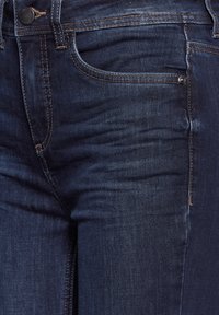 Jean en denim bleu foncé avec un design classique à cinq poches, des coutures subtiles et une texture lisse. Accents en métal sur le bouton et les rivets. 