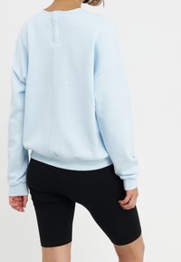 Sudadera azul clara de corte holgado, cuello redondo y puños de canalé, combinada con pantalones cortos negros. Textura suave, diseño minimalista.