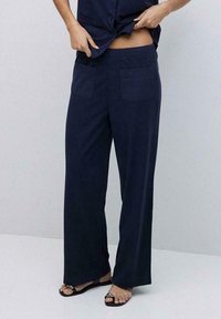 Pantalones de pierna ancha en color navy, confeccionados en una tela suave, con dos bolsillos traseros y una cintura alta. El dobladillo es ligeramente acampanado, lo que complementa unas sandalias de punta abierta.