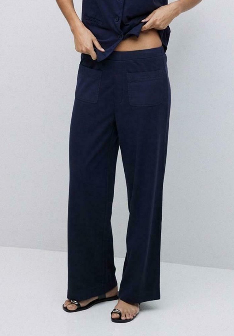 Pantalones de pierna ancha en color navy, confeccionados en una tela suave, con dos bolsillos traseros y una cintura alta. El dobladillo es ligeramente acampanado, lo que complementa unas sandalias de punta abierta.