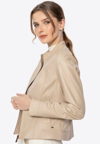 Beige leren jas met een aansluitend ontwerp, gewatteerde schouderaccenten, ritsluiting, zijzakken en een gladde textuur.