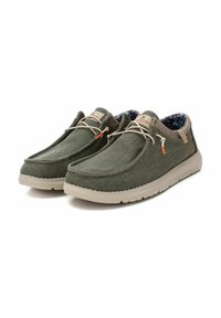 Zapatillas de lona verdes con un empeine texturizado, cordones beige y un interior de patrón contrastante. Presenta una suela de goma de color claro.