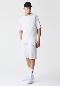 Light grey cotton t-shirt with a round neckline, paired with matching shorts. A black logo accent on the shirt and shorts, complemented by white sneakers.