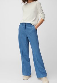 Ljusblå vida byxor i bomullsmix, med knäppning och två framfickor. Kombination med en krämfärgad tröja.