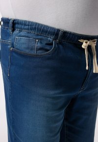 Pantalones jogger de mezclilla en azul oscuro con cinturilla elástica y cordón. Presentan un bolsillo trasero y una textura suave, ligeramente desgastada.