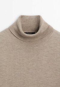 Pull en laine beige à col roulé tricoté avec col et épaules côtelés, plié soigneusement sur fond blanc.