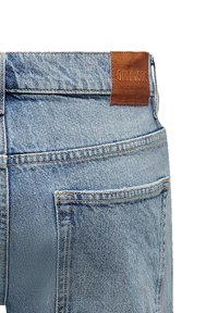 Jeans en denim bleu clair avec une finition texturée, dotés d'une étiquette en cuir à la taille et de poches arrière avec des détails de couture visibles.