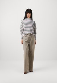 Striped, pale purple and green turtleneck sweater; light grey high-waisted jeans with a relaxed fit; flat sandals; minimal background.