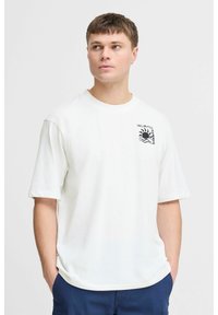 Hvid bomulds-t-shirt med korte ærmer, prydet med et sort grafisk design på venstre bryst med et sol- og bølgemønster.