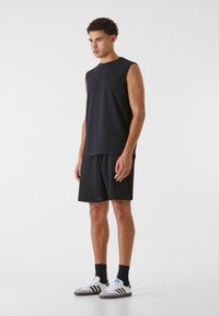 Schwarzes ärmelloses Oberteil mit rundem Ausschnitt, kombiniert mit schwarzen Shorts mit elastischem Bund. Gestylt mit weißen und grauen Sneakers.