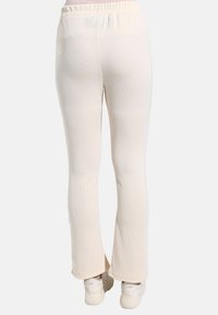 Geribbelde crèmekleurige broek met een elastische tailleband, uitlopende vorm en een zachte textuur, met een aansluitend pootontwerp en geen zichtbare zakken.
