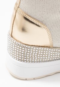 Tenisky s metalickým zlatým a bílým designem, s třpytivým podpatkem zdobeným rhinestones a textilním svrškem v krémové barvě.