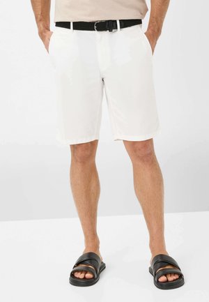 Shorts blancs avec un devant plat, des poches en biais et des ourlets roulés. Associés à des sandales noires à enfiler et à une ceinture tressée noire. Tissu lisse.