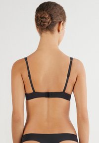 Černá podprsenka s nastavitelnými ramínky a zapínáním na háček a oko vzadu. Hladká textilie, minimalistický design a žádné viditelné ozdoby.