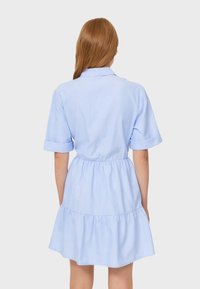 Abito camicia azzurro chiaro con maniche corte arrotolate, vita aderente e gonna a ruota a balze. Realizzato in tessuto morbido con una texture liscia.