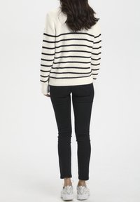 Suéter de punto en crema con rayas horizontales negras, combinado con jeans ajustados negros y zapatillas blancas. La textura parece suave y elástica.
