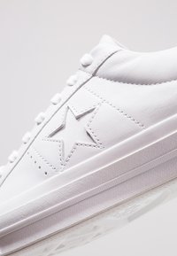 Baskets en cuir blanc avec un motif d'étoile, une texture lisse, un bout rond et une semelle en caoutchouc plate avec des motifs d'adhérence subtils.