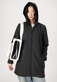 Veste noire imperméable avec fermeture éclair sur le devant, capuche et deux poches latérales, assortie à un sac texturé blanc et noir.
