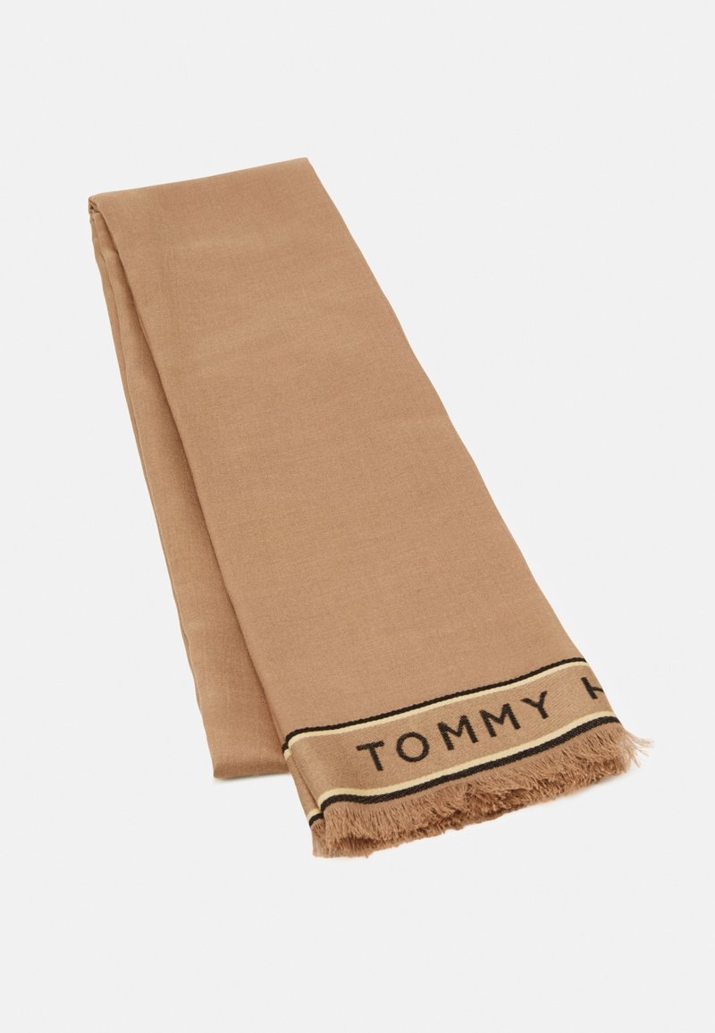 Écharpe beige pliée avec extrémités à franges et bande beige bordée de noir comportant un texte partiellement visible « TOMMY H ».