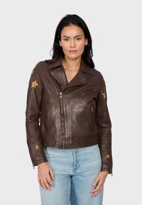Veste en cuir marron de style biker avec des accents en forme d'étoile dorée. Présente un col cranté, des poches zippées et un design court. Texture lisse.