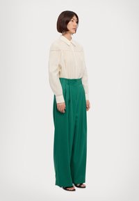 Cream cotton blouse with pintuck detailing, paired with high-waisted, wide-leg green trousers, and black sandals.
